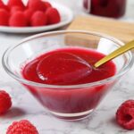 Coulis de frambuesa casero en un tazón con frambuesas frescas alrededor